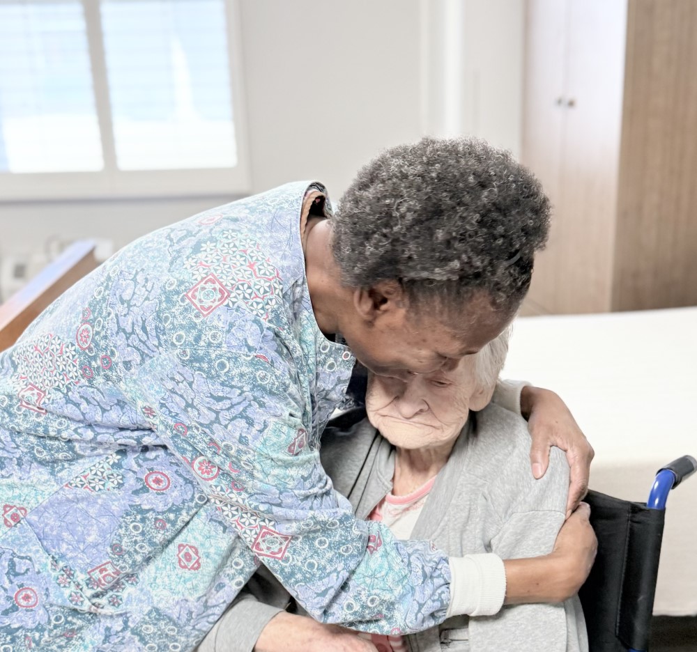 female nurse comforts female patient in wheelchair