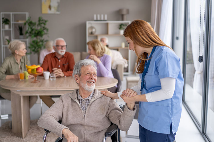 A nurse talks with an elderly man sitting in the lobby of a nursing facility in Bossier City