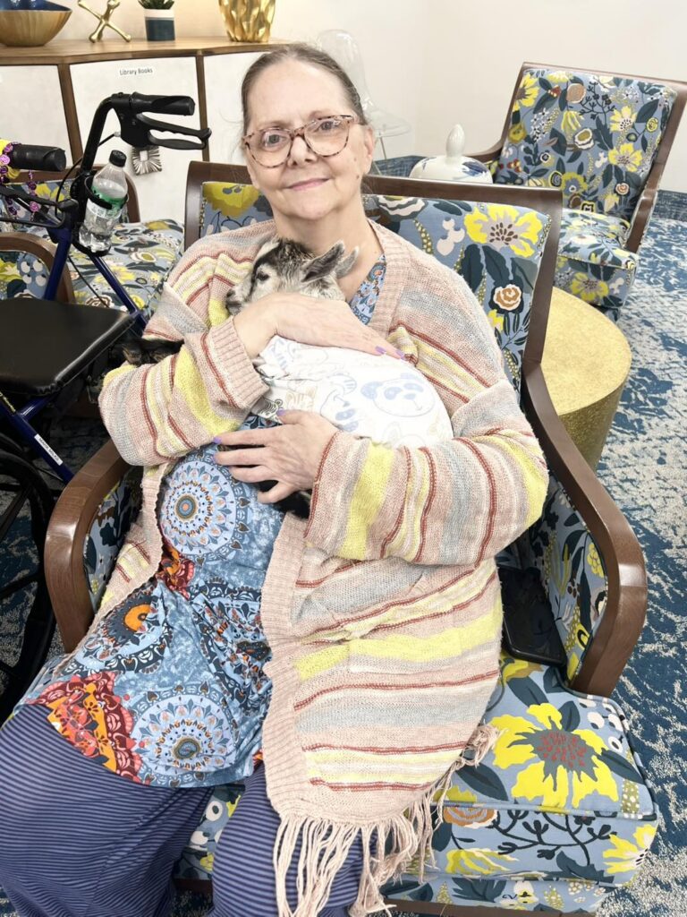 Resident holding a baby goat during a weekly activity at Pilgrim Manor