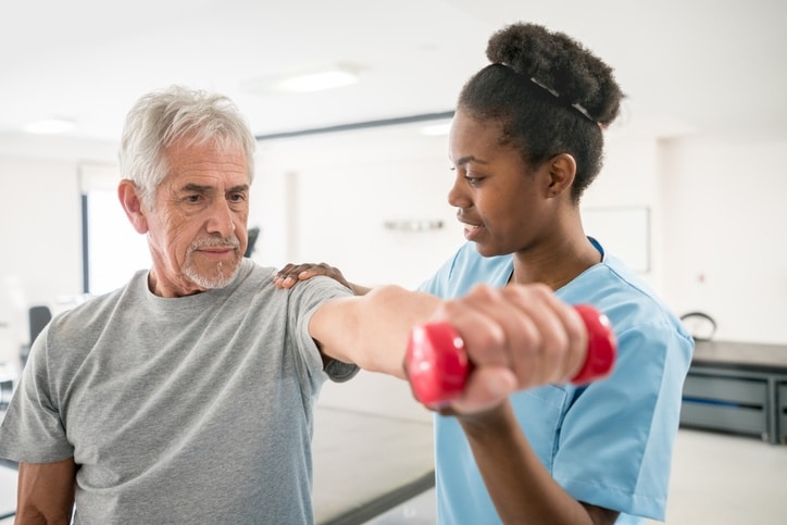 Caregiver guiding a senior man with weight lifting during rehabilitation