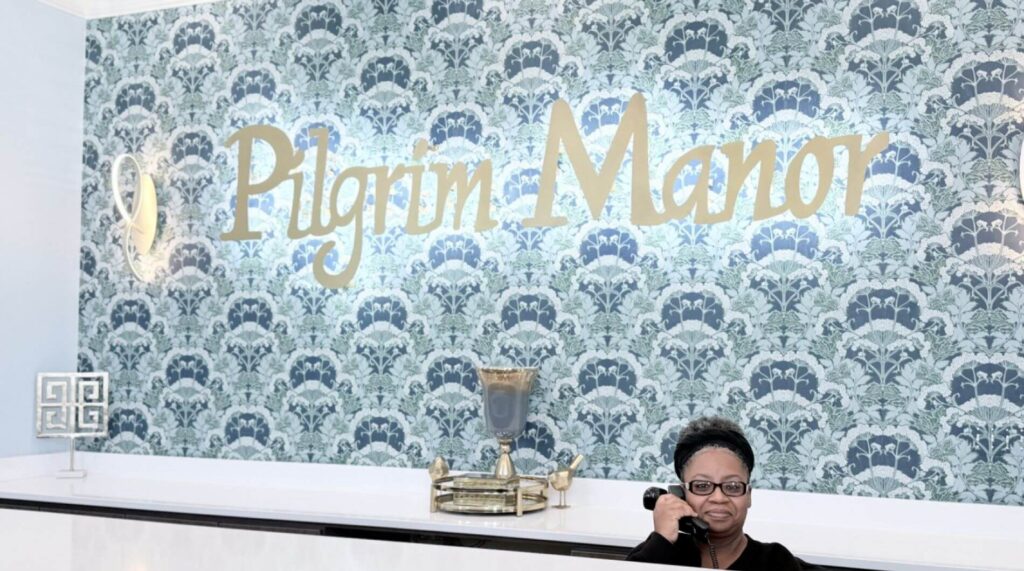 Receptionist on the phone by the Pilgrim Manor sign